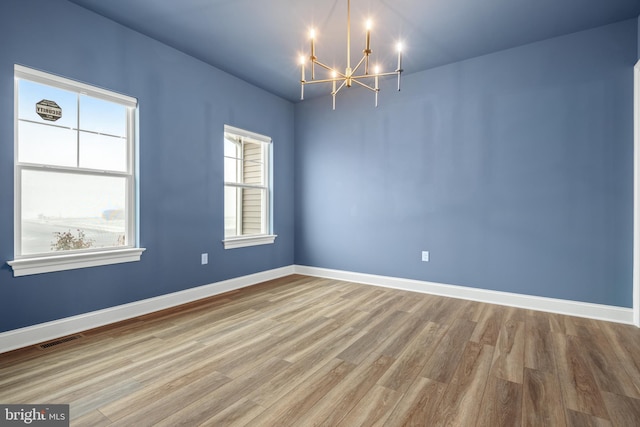 empty room with a wealth of natural light, hardwood / wood-style floors, and a chandelier