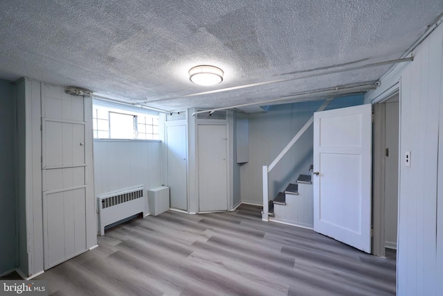 basement with a textured ceiling, radiator heating unit, and wood-type flooring