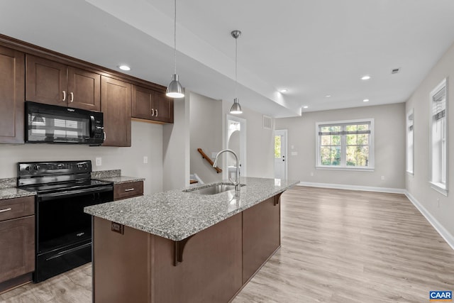 kitchen with light stone countertops, black appliances, sink, light wood-type flooring, and a kitchen island with sink