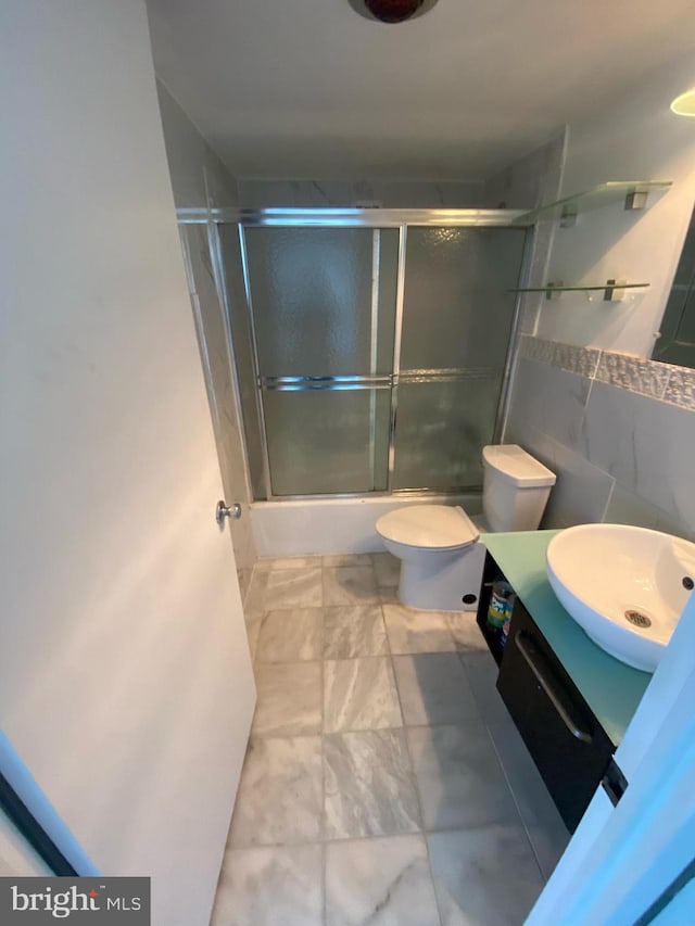 bathroom featuring shower / bath combination with glass door, toilet, tile walls, vanity, and marble finish floor