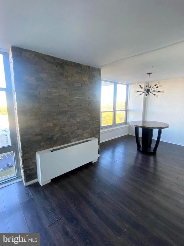 unfurnished living room featuring dark wood-type flooring, a notable chandelier, and baseboard heating