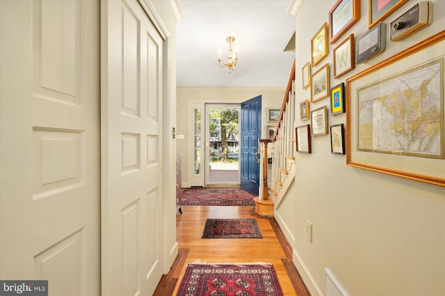 doorway with hardwood / wood-style flooring, ornamental molding, and an inviting chandelier