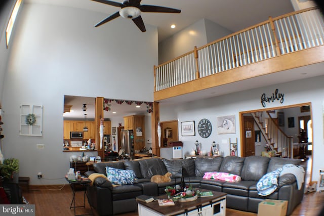 living room featuring hardwood / wood-style flooring, ceiling fan, and a towering ceiling