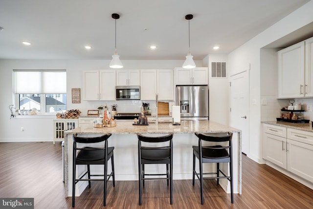 kitchen with dark hardwood / wood-style flooring, hanging light fixtures, stainless steel appliances, white cabinets, and a kitchen island with sink