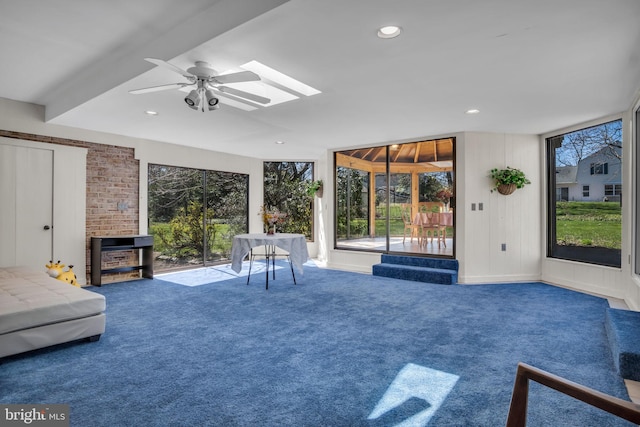 unfurnished living room with beam ceiling, ceiling fan, carpet flooring, and a skylight