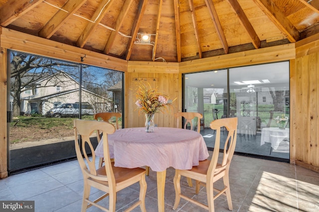 dining room featuring light tile patterned flooring, vaulted ceiling, and wooden walls