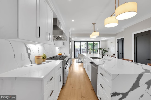 kitchen with wall chimney range hood, white cabinets, appliances with stainless steel finishes, and a sink