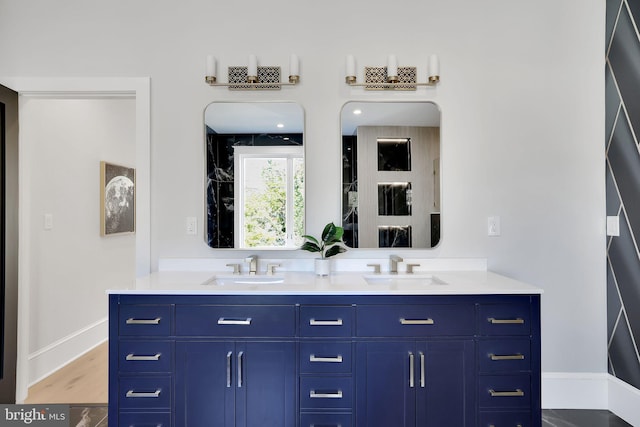 full bath with baseboards, double vanity, a sink, and wood finished floors