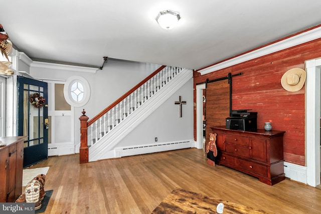 foyer entrance featuring a baseboard radiator, wooden walls, a barn door, and light hardwood / wood-style flooring