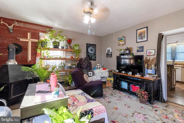 living room featuring light hardwood / wood-style flooring, a wood stove, sink, and ceiling fan