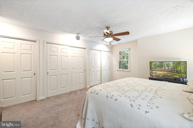 carpeted bedroom featuring a textured ceiling, two closets, and ceiling fan