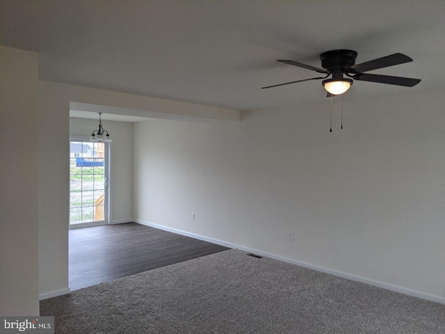 spare room with dark wood-type flooring and ceiling fan with notable chandelier