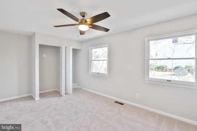 unfurnished bedroom with light carpet, two closets, and ceiling fan