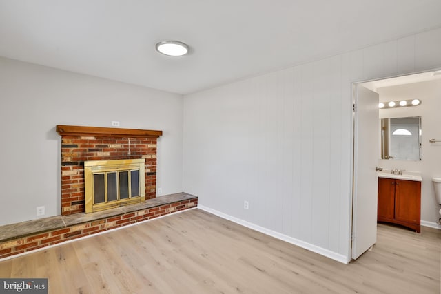 unfurnished living room featuring sink, a fireplace, and light wood-type flooring