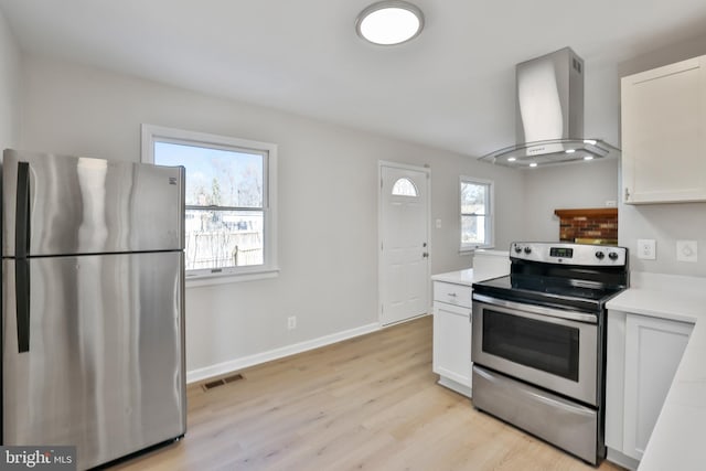 kitchen with white cabinetry, light hardwood / wood-style floors, wall chimney exhaust hood, and appliances with stainless steel finishes