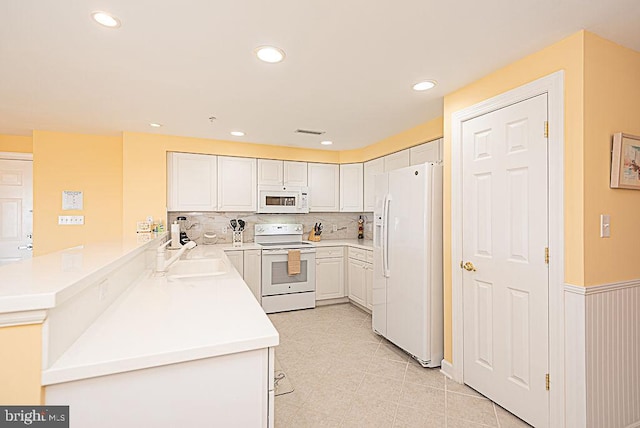 kitchen with kitchen peninsula, sink, white cabinets, white appliances, and tasteful backsplash