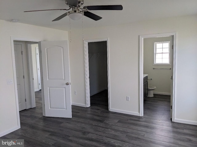 unfurnished bedroom with a closet, a spacious closet, ensuite bath, dark hardwood / wood-style flooring, and ceiling fan