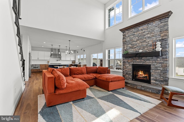 living room with an inviting chandelier, a fireplace, wood-type flooring, and a high ceiling