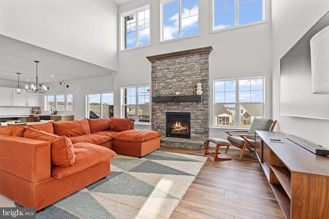 living room featuring a stone fireplace, a notable chandelier, a high ceiling, and light wood-type flooring