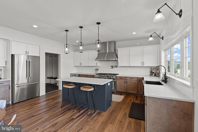 kitchen with premium appliances, wall chimney range hood, sink, a kitchen island, and white cabinets