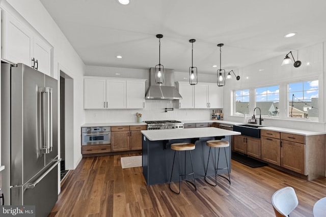 kitchen with wall chimney exhaust hood, white cabinets, stainless steel appliances, and a kitchen island