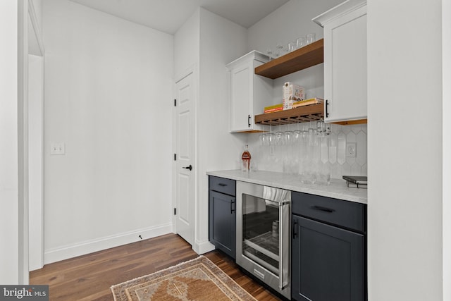 bar with dark wood-type flooring, white cabinetry, beverage cooler, and backsplash