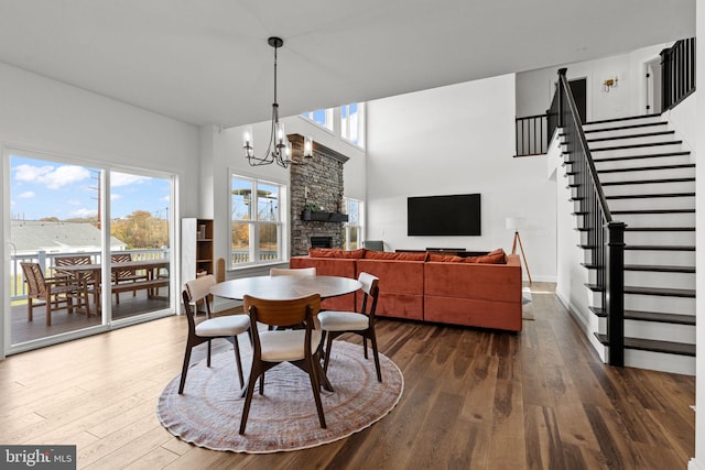 dining area featuring a stone fireplace, a notable chandelier, a high ceiling, and dark hardwood / wood-style flooring