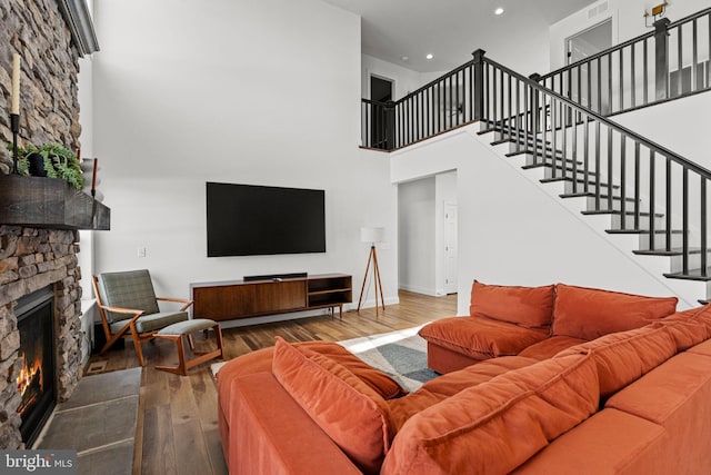 living room with a stone fireplace, hardwood / wood-style floors, and a towering ceiling