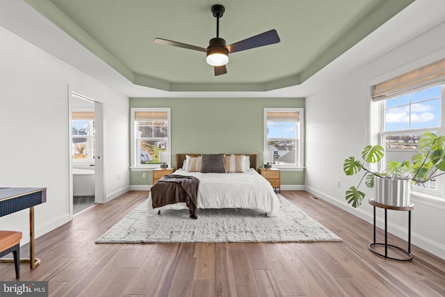 bedroom with multiple windows, ensuite bath, wood-type flooring, and ceiling fan