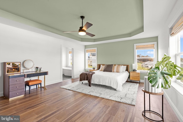 bedroom with ensuite bathroom, ceiling fan, a raised ceiling, and dark hardwood / wood-style flooring