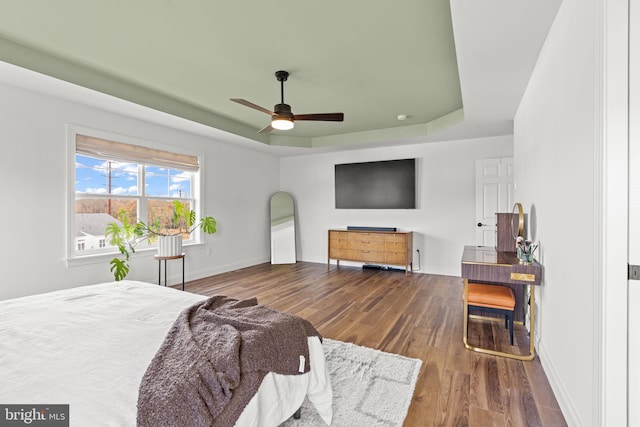 bedroom with a raised ceiling, wood-type flooring, and ceiling fan