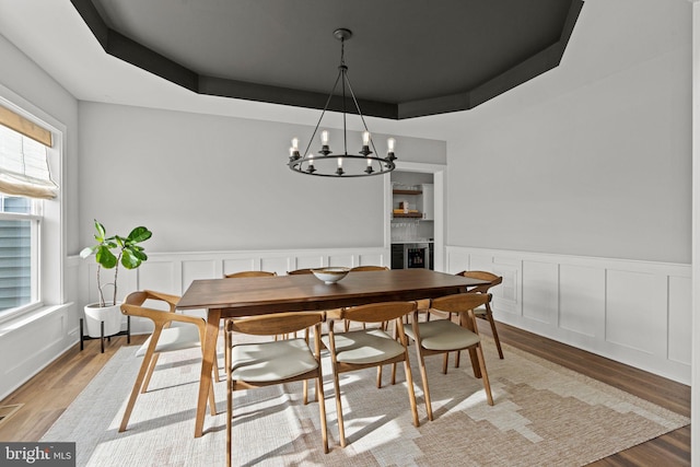 dining area with hardwood / wood-style flooring, a healthy amount of sunlight, a chandelier, and a raised ceiling