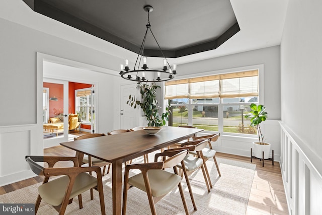 dining space featuring an inviting chandelier, light hardwood / wood-style flooring, and a raised ceiling