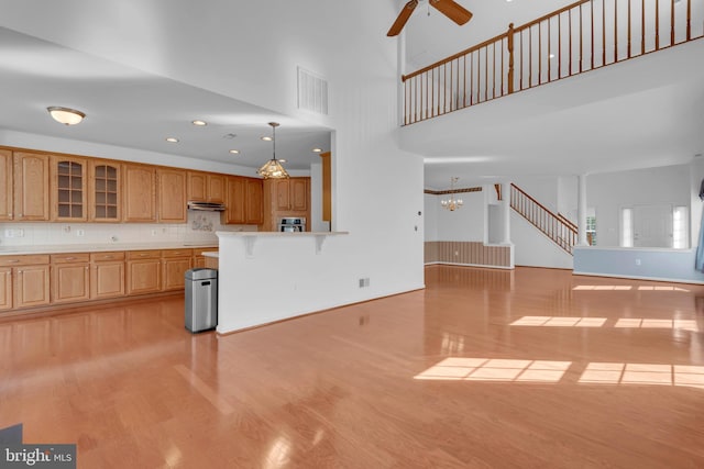 kitchen with a towering ceiling, ceiling fan with notable chandelier, hanging light fixtures, decorative backsplash, and light hardwood / wood-style flooring