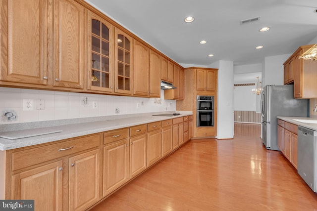 kitchen with tasteful backsplash, light stone countertops, light wood-type flooring, stainless steel appliances, and a chandelier