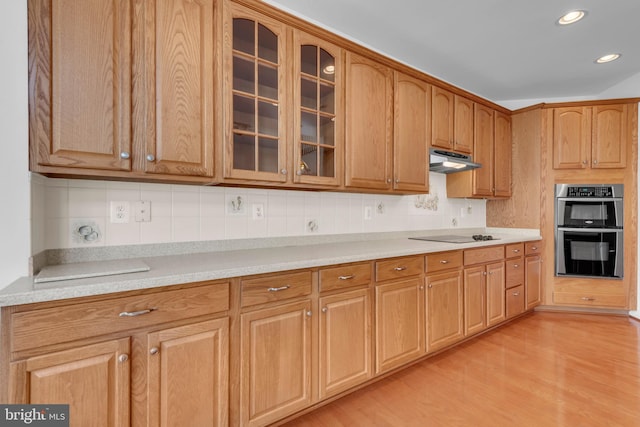 kitchen with black electric stovetop, decorative backsplash, double oven, and light wood-type flooring