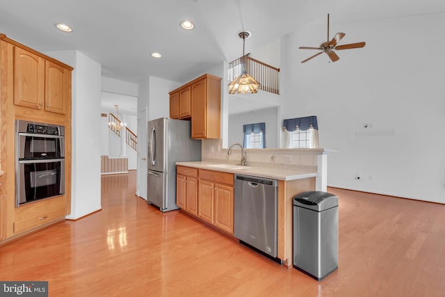 kitchen featuring sink, light wood-type flooring, stainless steel appliances, pendant lighting, and high vaulted ceiling