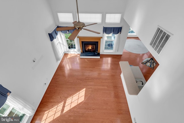 unfurnished living room with a high ceiling, wood-type flooring, a healthy amount of sunlight, and ceiling fan