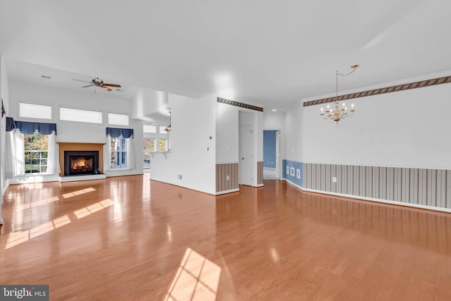 unfurnished living room featuring hardwood / wood-style flooring, ceiling fan with notable chandelier, and plenty of natural light