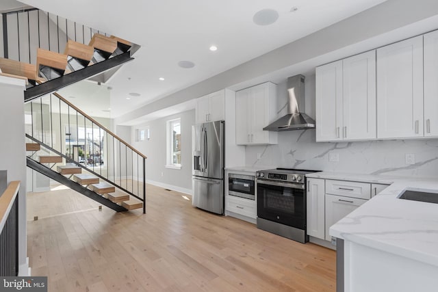 kitchen featuring wall chimney range hood, light hardwood / wood-style flooring, white cabinetry, appliances with stainless steel finishes, and tasteful backsplash