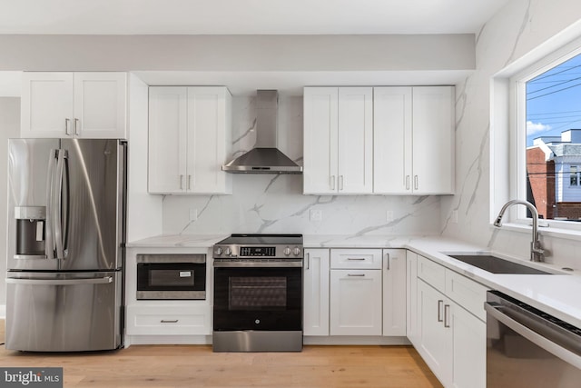 kitchen with appliances with stainless steel finishes, wall chimney exhaust hood, sink, and a wealth of natural light