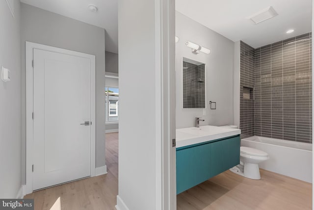 full bathroom featuring tiled shower / bath, vanity, hardwood / wood-style flooring, and toilet