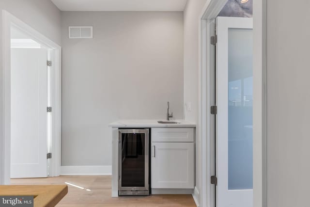 bar featuring white cabinetry, light hardwood / wood-style flooring, wine cooler, and sink