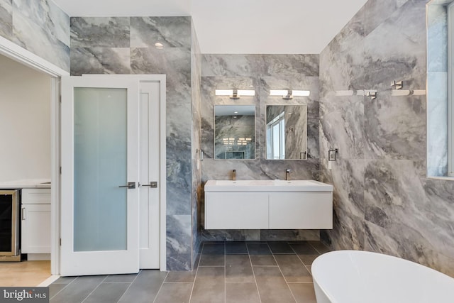 bathroom with beverage cooler, tile walls, vanity, a tub to relax in, and tile patterned flooring