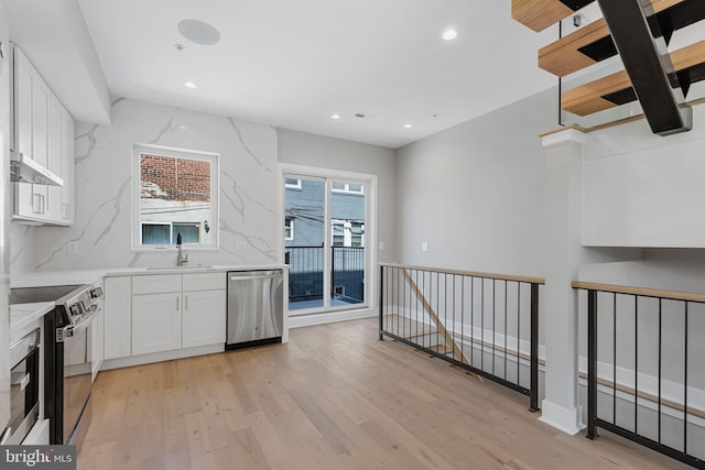 kitchen featuring light stone counters, appliances with stainless steel finishes, white cabinetry, light hardwood / wood-style flooring, and sink