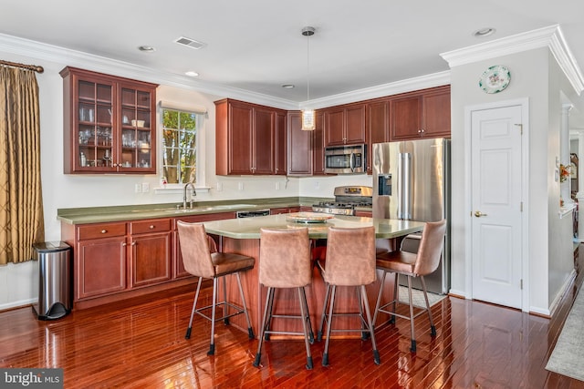 kitchen with dark wood-type flooring, crown molding, a center island, pendant lighting, and appliances with stainless steel finishes