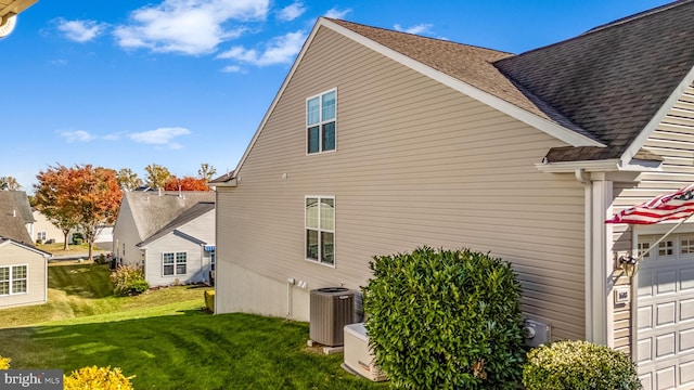 view of side of property featuring central air condition unit, a lawn, and a garage