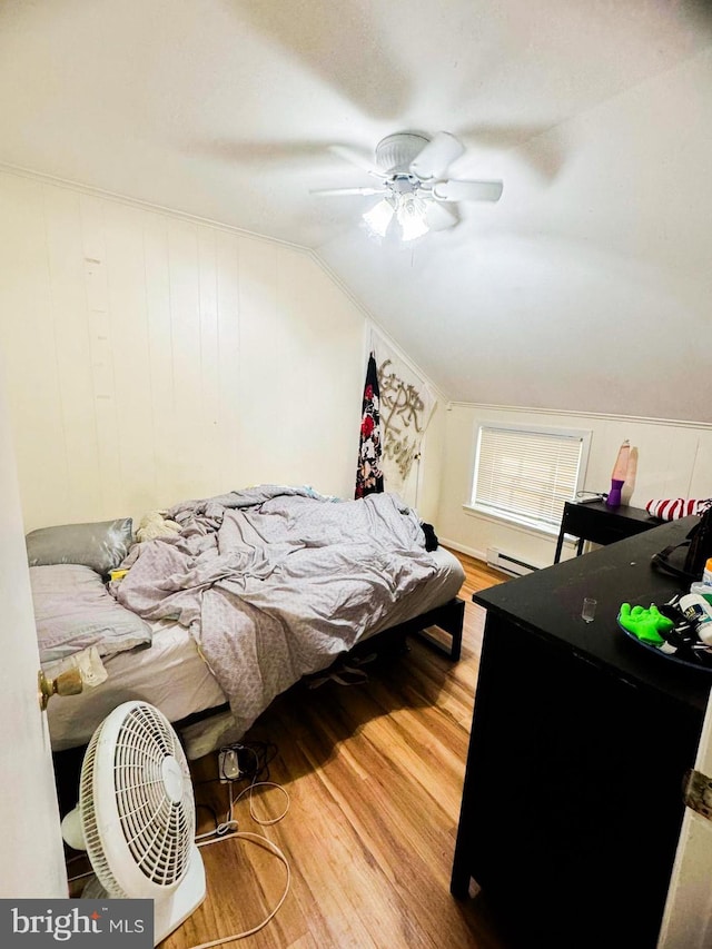 bedroom with wood-type flooring, wooden walls, vaulted ceiling, baseboard heating, and ceiling fan