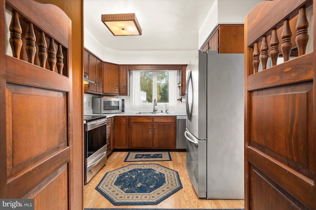 kitchen featuring light wood-style flooring, a sink, appliances with stainless steel finishes, light countertops, and exhaust hood