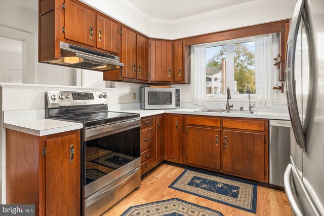 kitchen featuring a sink, stainless steel appliances, under cabinet range hood, light wood-type flooring, and light countertops